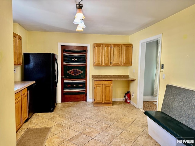 kitchen featuring freestanding refrigerator, light tile patterned flooring, light countertops, dishwashing machine, and built in study area