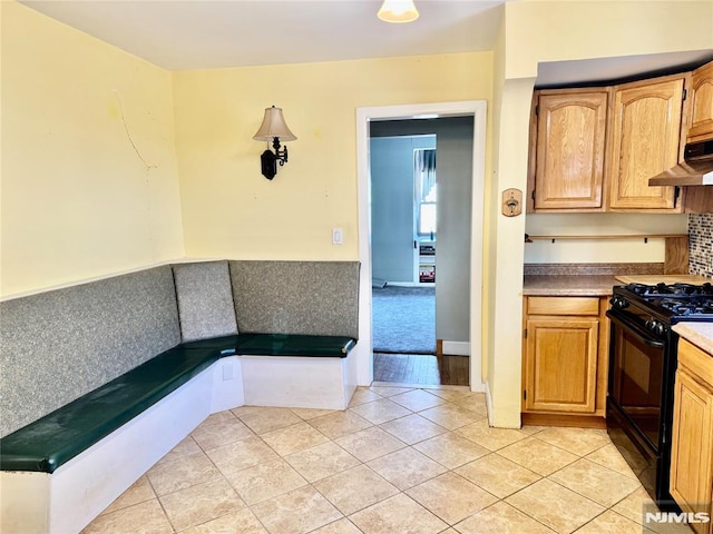 kitchen featuring under cabinet range hood, light tile patterned floors, and gas stove