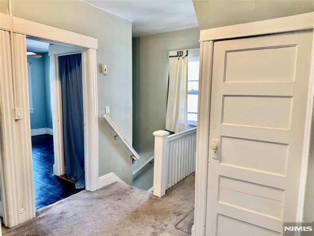 hall featuring baseboards, an upstairs landing, and carpet floors