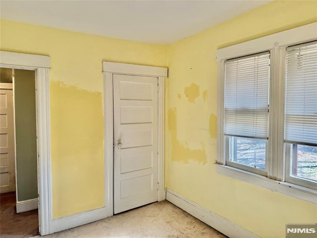 unfurnished bedroom with baseboard heating, light colored carpet, and baseboards