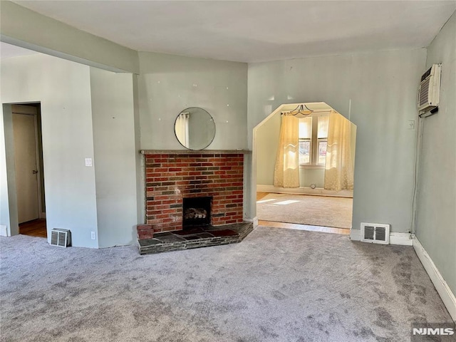 unfurnished living room featuring a fireplace, visible vents, carpet floors, and a wall mounted AC