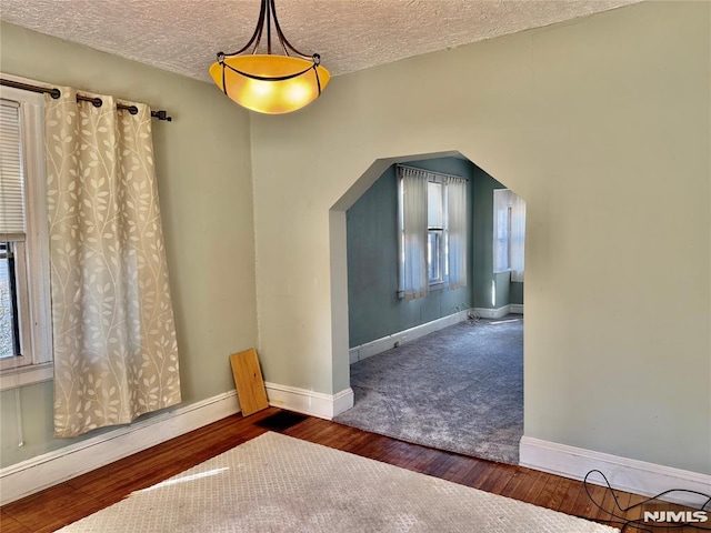 interior space with a baseboard heating unit, wood finished floors, arched walkways, and baseboards