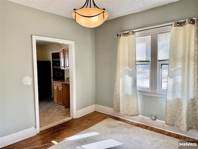 spare room with wood finished floors, baseboards, and a textured ceiling