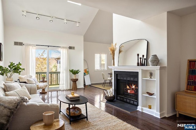 living room featuring visible vents, a warm lit fireplace, lofted ceiling, and wood finished floors