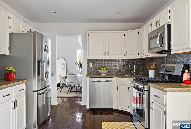 kitchen with a sink, backsplash, white cabinetry, stainless steel appliances, and dark wood-style flooring