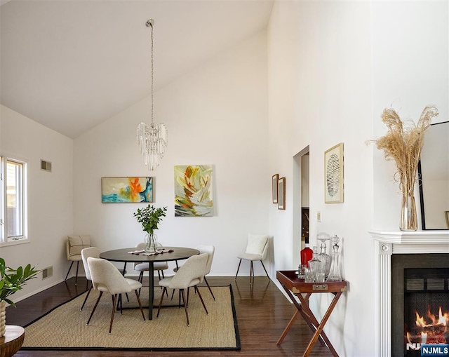 dining area featuring visible vents, high vaulted ceiling, an inviting chandelier, a lit fireplace, and dark wood-type flooring