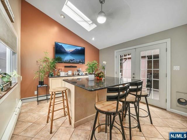 kitchen with a kitchen bar, lofted ceiling with skylight, a center island, french doors, and light tile patterned floors