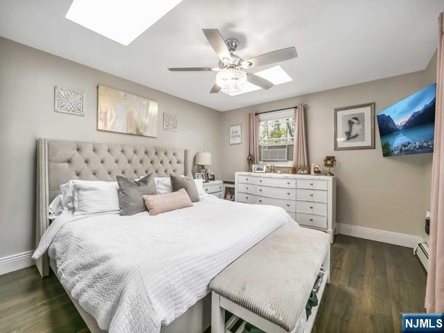 bedroom featuring a skylight, a ceiling fan, baseboards, and dark wood-style flooring