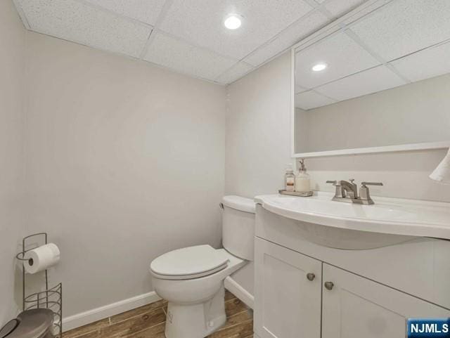 bathroom with baseboards, wood tiled floor, a drop ceiling, toilet, and vanity