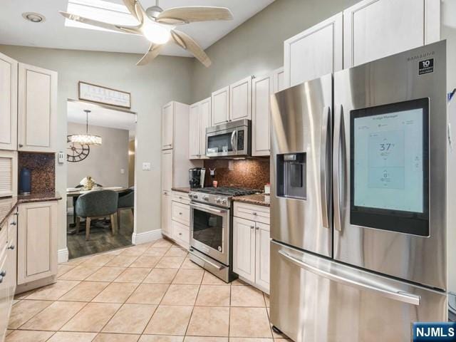 kitchen featuring decorative backsplash, ceiling fan with notable chandelier, light tile patterned flooring, white cabinets, and stainless steel appliances