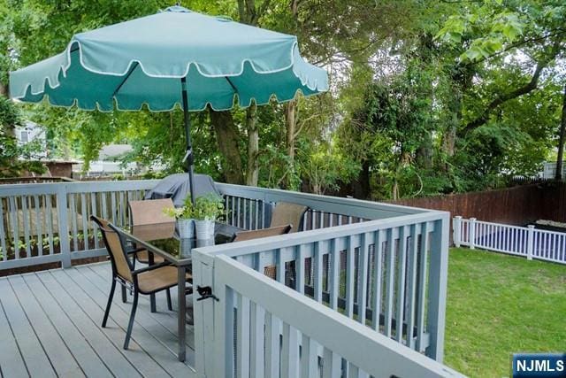 wooden terrace featuring a lawn, outdoor dining area, and fence