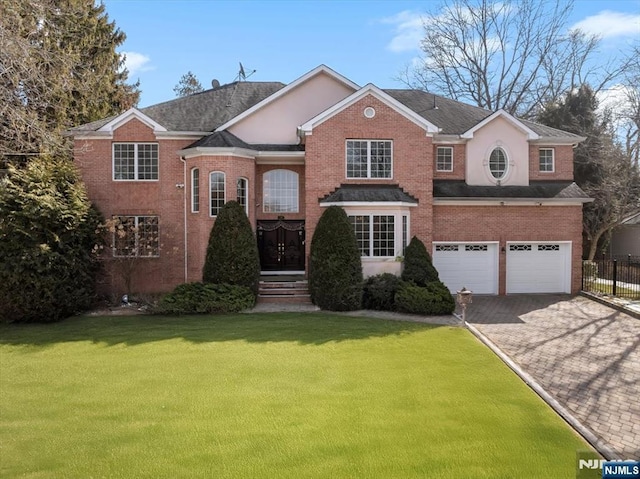 traditional-style home featuring a front lawn, decorative driveway, fence, a garage, and brick siding