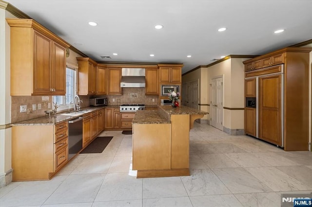 kitchen with built in appliances, dark stone countertops, a kitchen island, and wall chimney range hood