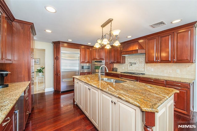 kitchen featuring visible vents, dark wood-type flooring, premium range hood, built in appliances, and a sink