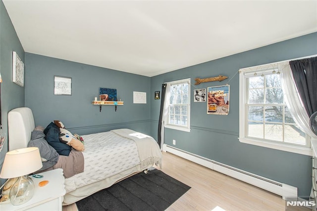 bedroom featuring a baseboard heating unit, multiple windows, and wood finished floors