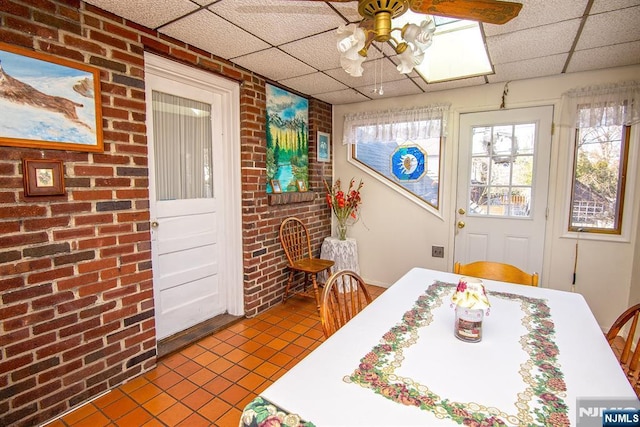 dining area featuring dark tile patterned floors, brick wall, a paneled ceiling, and a ceiling fan