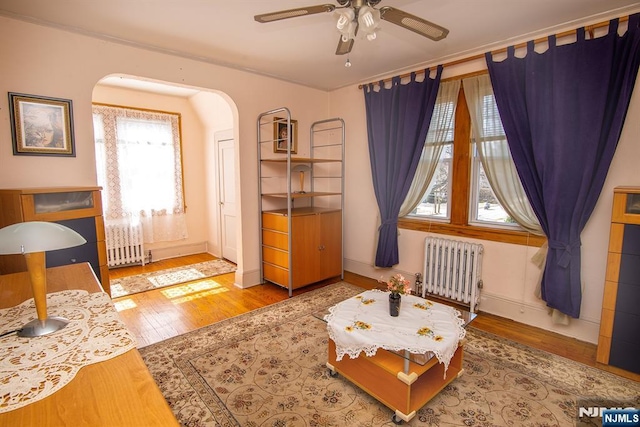 living area with arched walkways, a ceiling fan, wood finished floors, and radiator heating unit