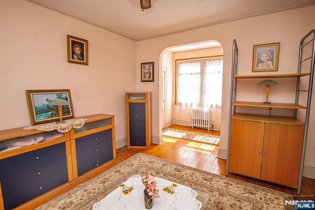 foyer entrance with arched walkways, light wood-style flooring, radiator, and baseboards