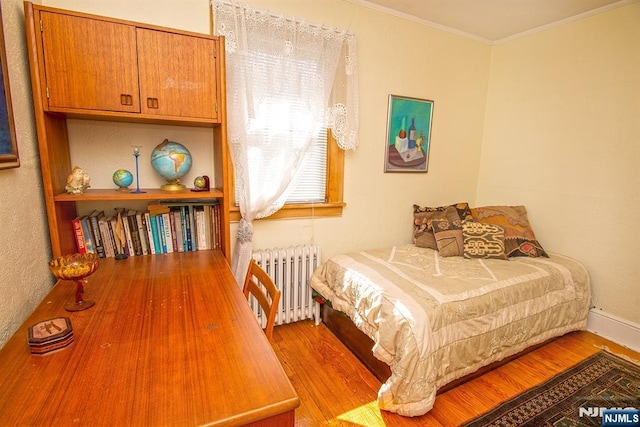 bedroom with ornamental molding, radiator heating unit, and wood finished floors