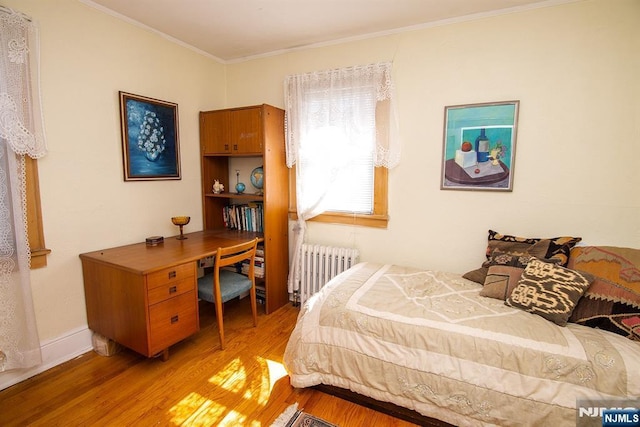 bedroom with crown molding, radiator heating unit, light wood-style floors, and baseboards