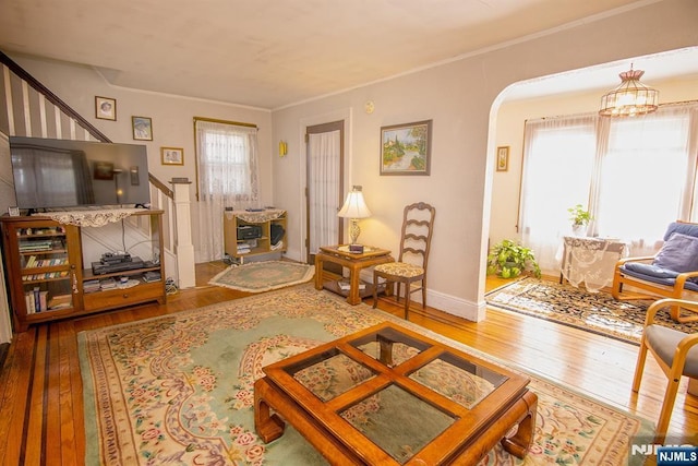 living area with stairway, baseboards, arched walkways, ornamental molding, and hardwood / wood-style flooring