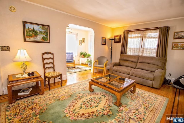 living area featuring baseboards, arched walkways, hardwood / wood-style floors, and ornamental molding