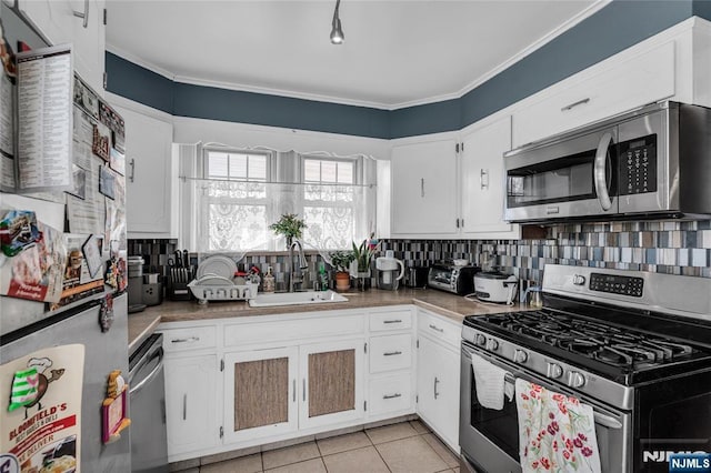 kitchen with a sink, appliances with stainless steel finishes, white cabinets, light tile patterned floors, and decorative backsplash