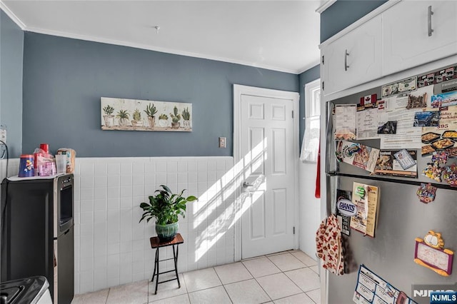 kitchen with crown molding, light tile patterned floors, freestanding refrigerator, white cabinets, and tile walls