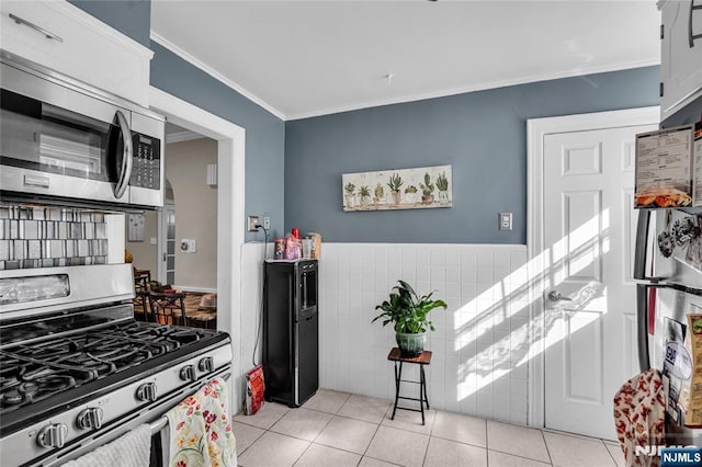 kitchen featuring stainless steel appliances, arched walkways, tile walls, light tile patterned flooring, and crown molding