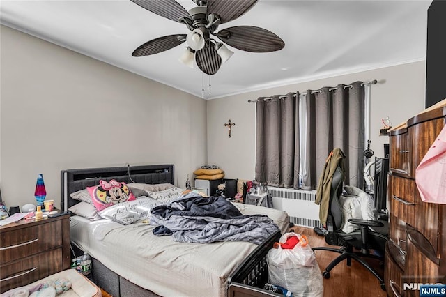 bedroom with radiator, wood finished floors, and a ceiling fan