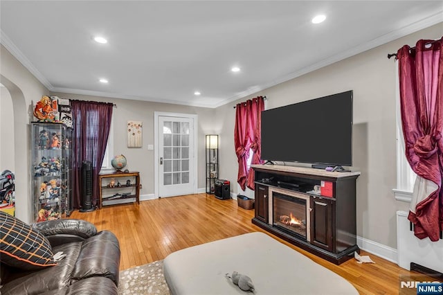 living area with light wood finished floors, ornamental molding, recessed lighting, arched walkways, and a glass covered fireplace