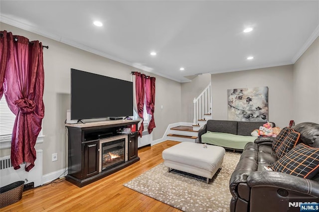 living area featuring baseboards, stairs, ornamental molding, light wood-style floors, and a glass covered fireplace