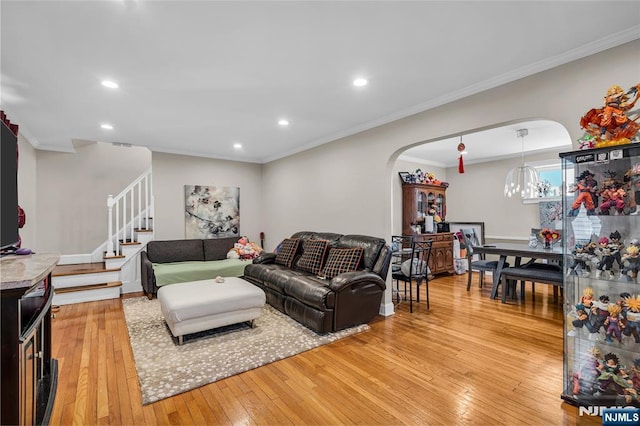 living room with stairway, arched walkways, light wood-style floors, and crown molding