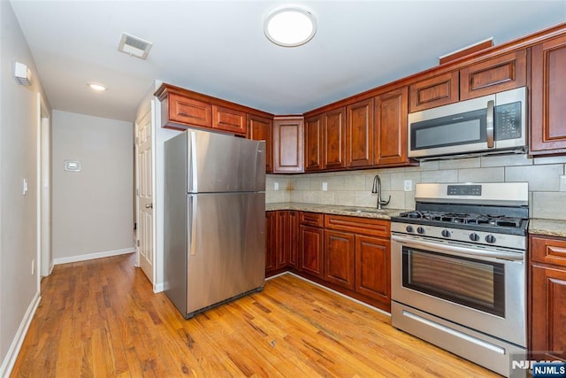 kitchen featuring a sink, stainless steel appliances, light wood-style floors, and backsplash