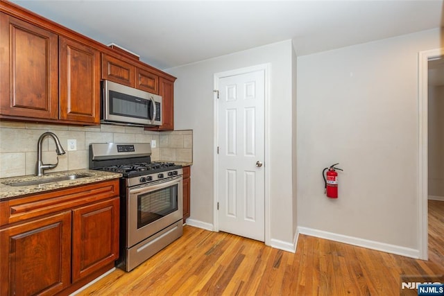 kitchen with light stone countertops, a sink, decorative backsplash, stainless steel appliances, and light wood-type flooring