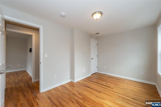 empty room with light wood-style flooring, visible vents, and baseboards