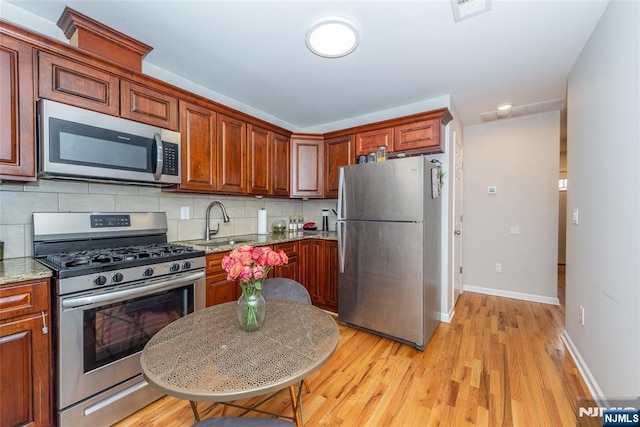 kitchen featuring baseboards, a sink, light wood-style floors, appliances with stainless steel finishes, and tasteful backsplash