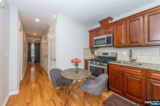 kitchen with a sink, stainless steel appliances, tasteful backsplash, and light wood-style flooring