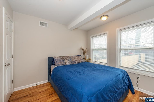 bedroom with beamed ceiling, wood finished floors, visible vents, and baseboards