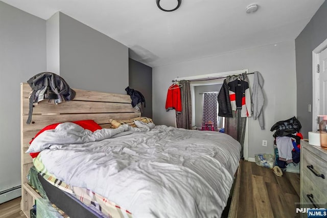 bedroom with a baseboard heating unit and wood finished floors