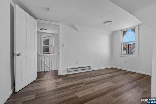 empty room with a baseboard heating unit, baseboards, and wood finished floors