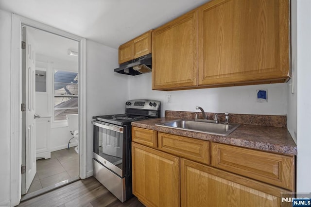 kitchen with under cabinet range hood, dark countertops, stainless steel electric range, and a sink