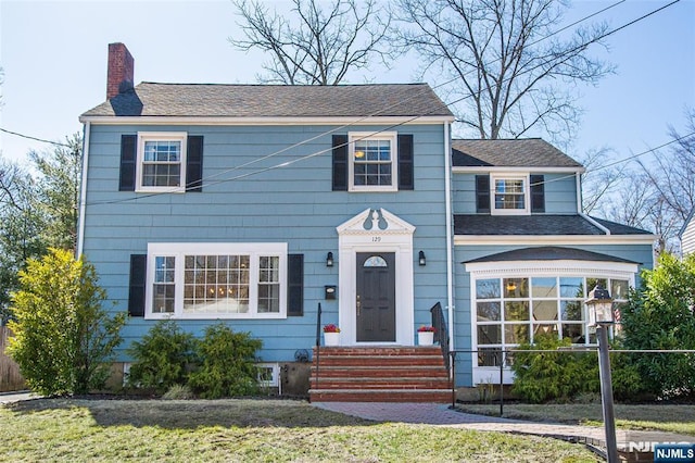 colonial inspired home featuring a chimney and a front lawn