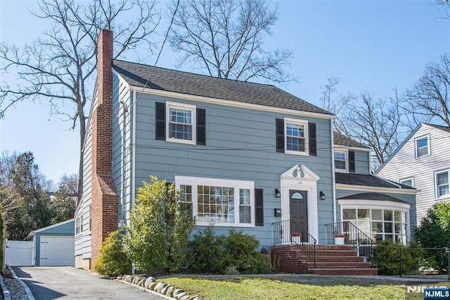 colonial house with an outbuilding, a detached garage, and a chimney