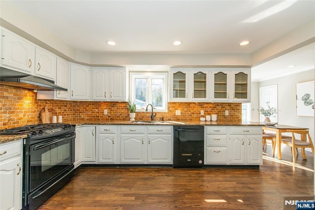 kitchen featuring glass insert cabinets, dark wood-type flooring, dark stone countertops, black appliances, and a sink