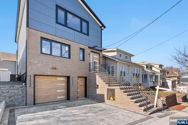 view of front facade with brick siding, stairs, central AC unit, decorative driveway, and a garage