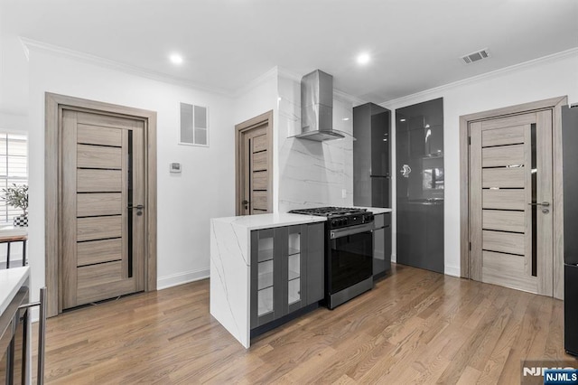 kitchen featuring gas range, wall chimney range hood, light wood-style floors, and visible vents