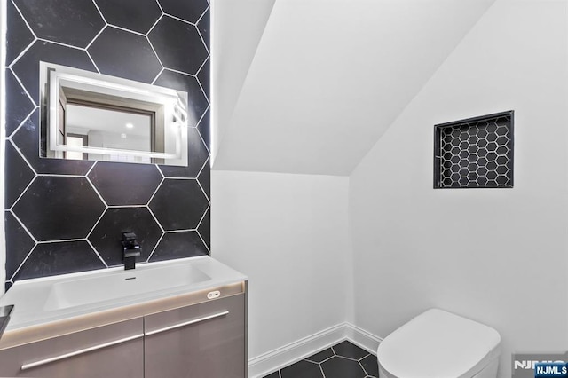 bathroom with vanity, baseboards, tile patterned flooring, vaulted ceiling, and toilet