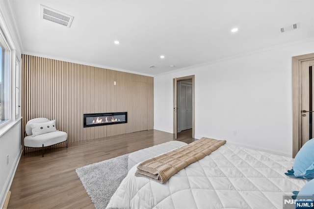 bedroom with a glass covered fireplace, wood finished floors, visible vents, and ornamental molding