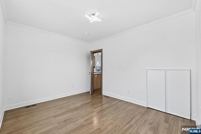 empty room with crown molding, wood finished floors, baseboards, and visible vents